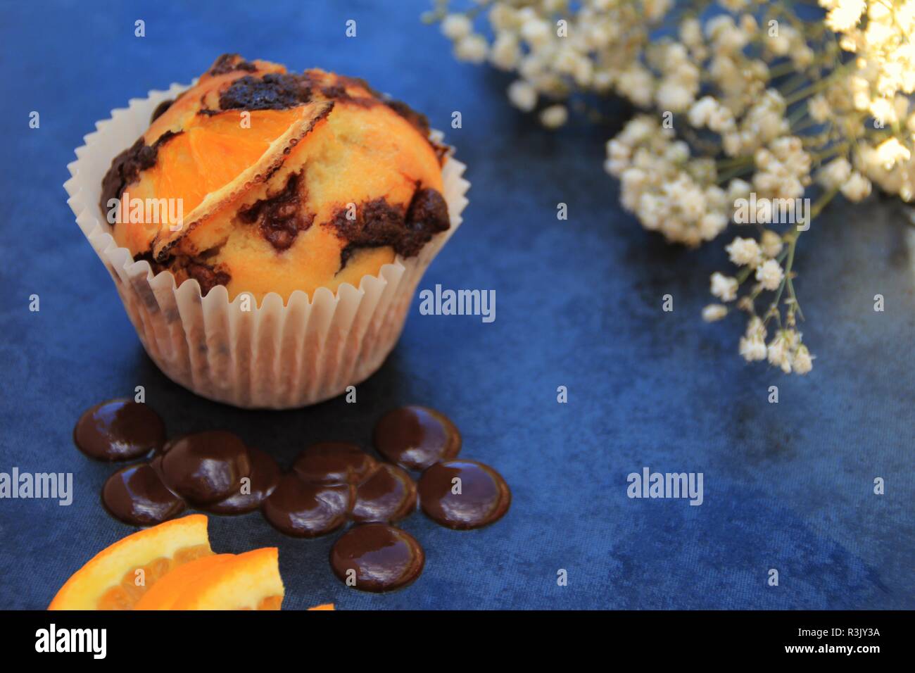 Arancione e muffin al cioccolato. Photo shot su piastrelle in ardesia con fiori come parte del sostegno in aggiunta con alcuni elementi di ingrediente del muffin Foto Stock