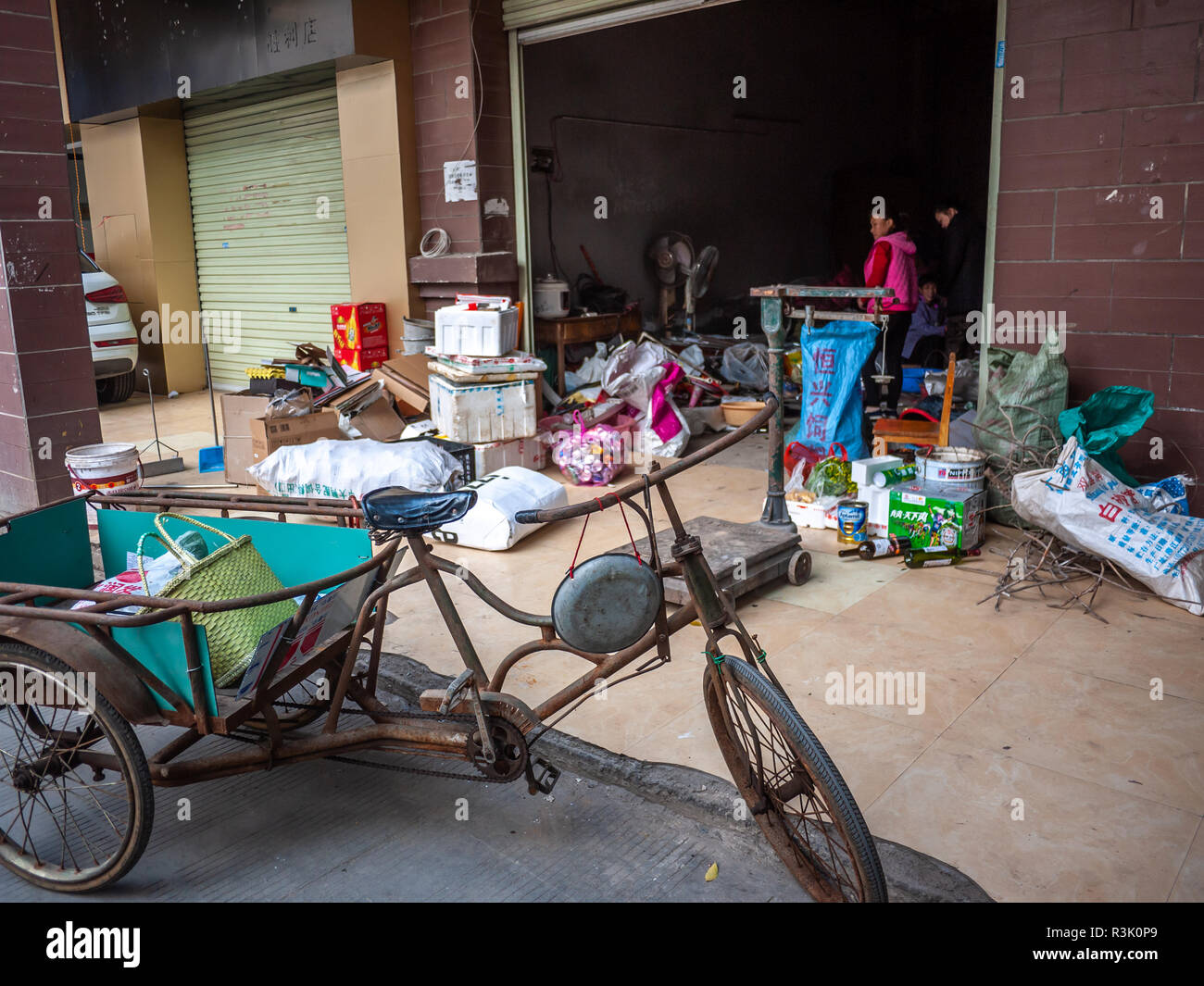 Un triciclo parcheggiato a fronte di un privato la raccolta dei rifiuti shop. Il proprietario fa i soldi con la raccolta di rifiuti porta a porta e rivenderli. Foto Stock