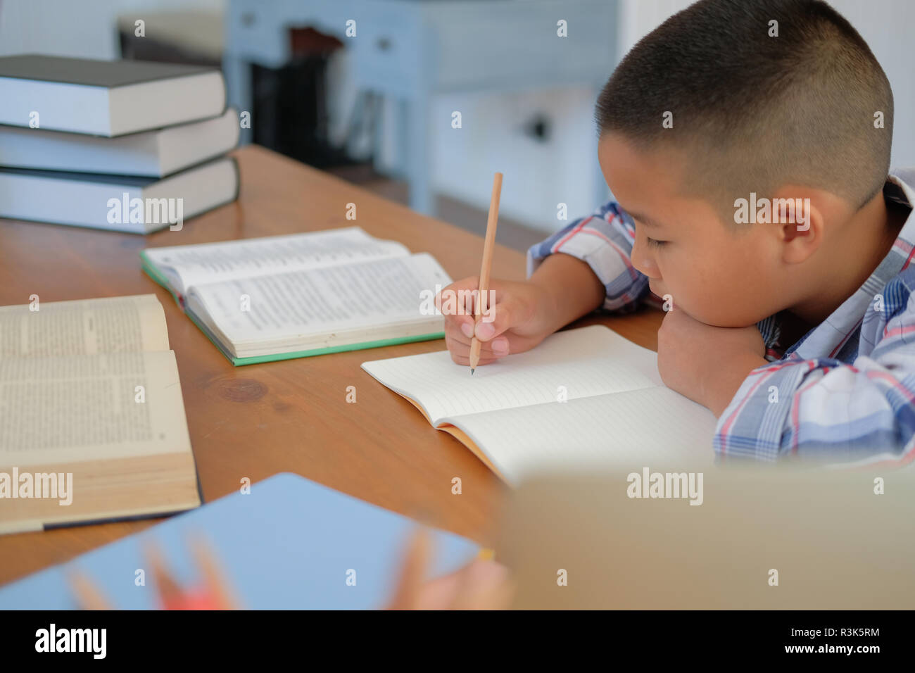 Giovane poco asian kid boy schoolboy iscritto il disegno sul notebook. bambini a fare i compiti. infanzia formazione Foto Stock