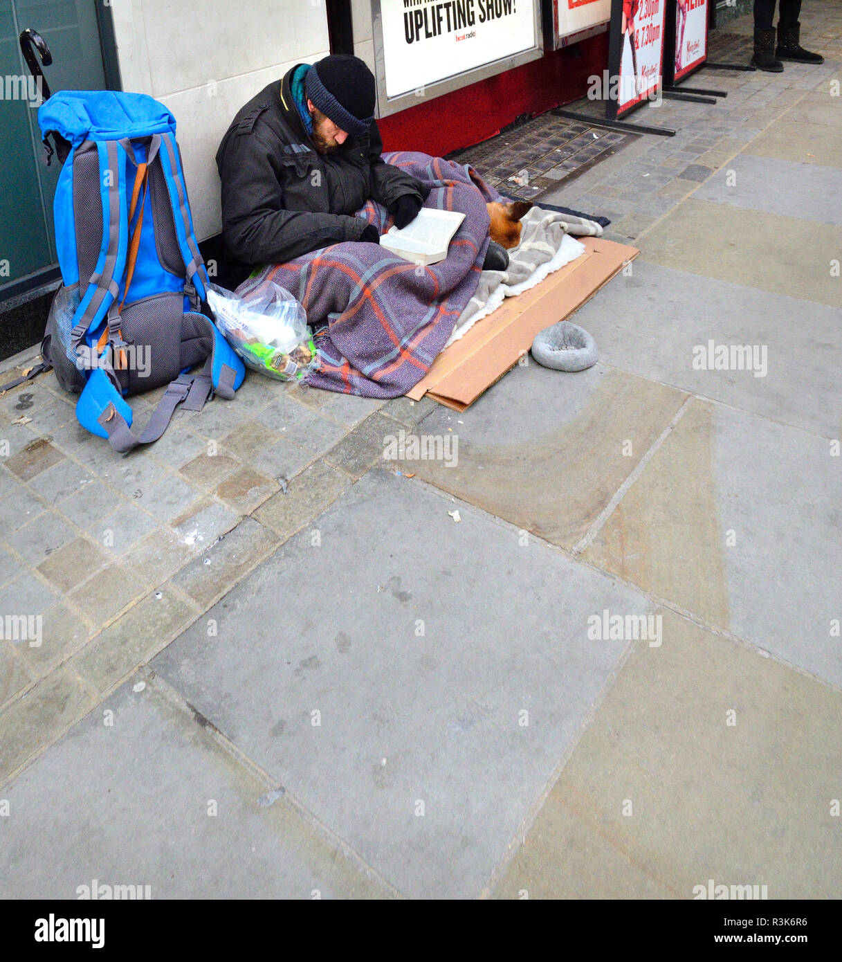 Uomo senza tetto con un cane, la lettura di un libro in The Strand, Londra, Inghilterra, Regno Unito. Foto Stock