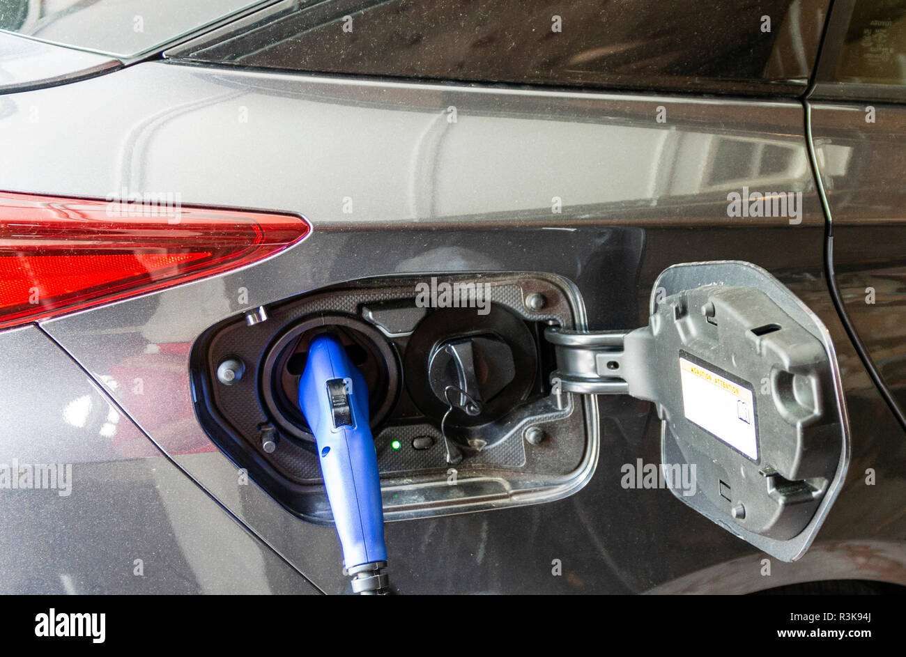 Un auto elettrica ibrida è collegato alla presa di corrente a casa con un blu del connettore elettrico. Foto Stock