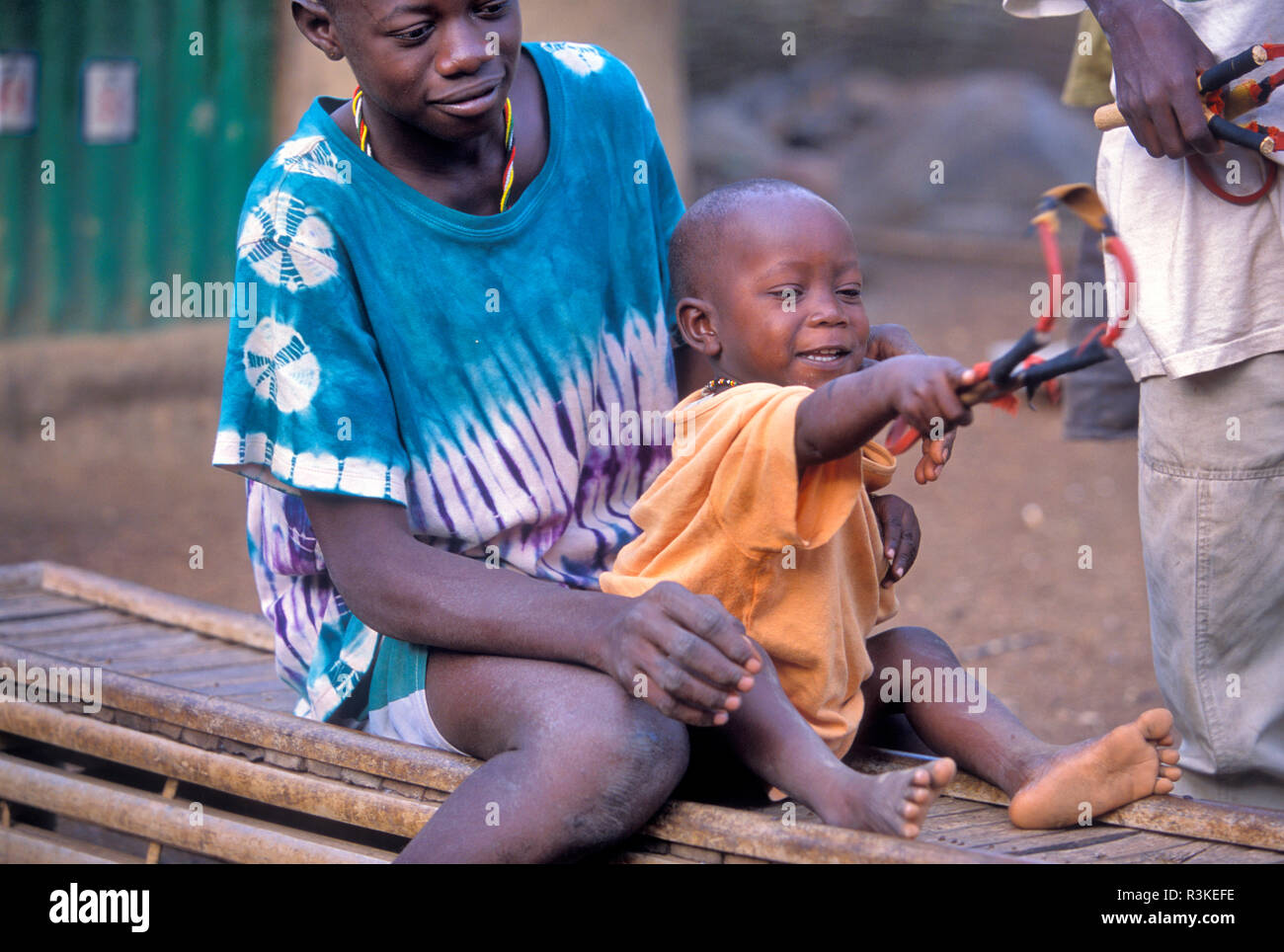 I vecchi insegnamento ragazzo giovane ragazzo a sparare Sling Shot in tribù Bedik villaggio di Iwol, Senegal. Foto Stock