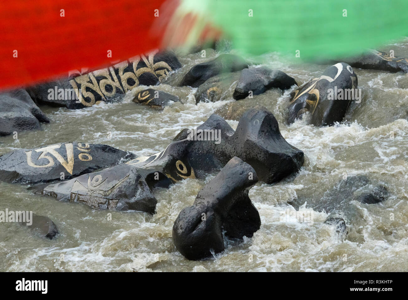 Rocce dipinte con parole di preghiera e la preghiera di bandiere nel fiume, Tagong, western Sichuan, Cina Foto Stock