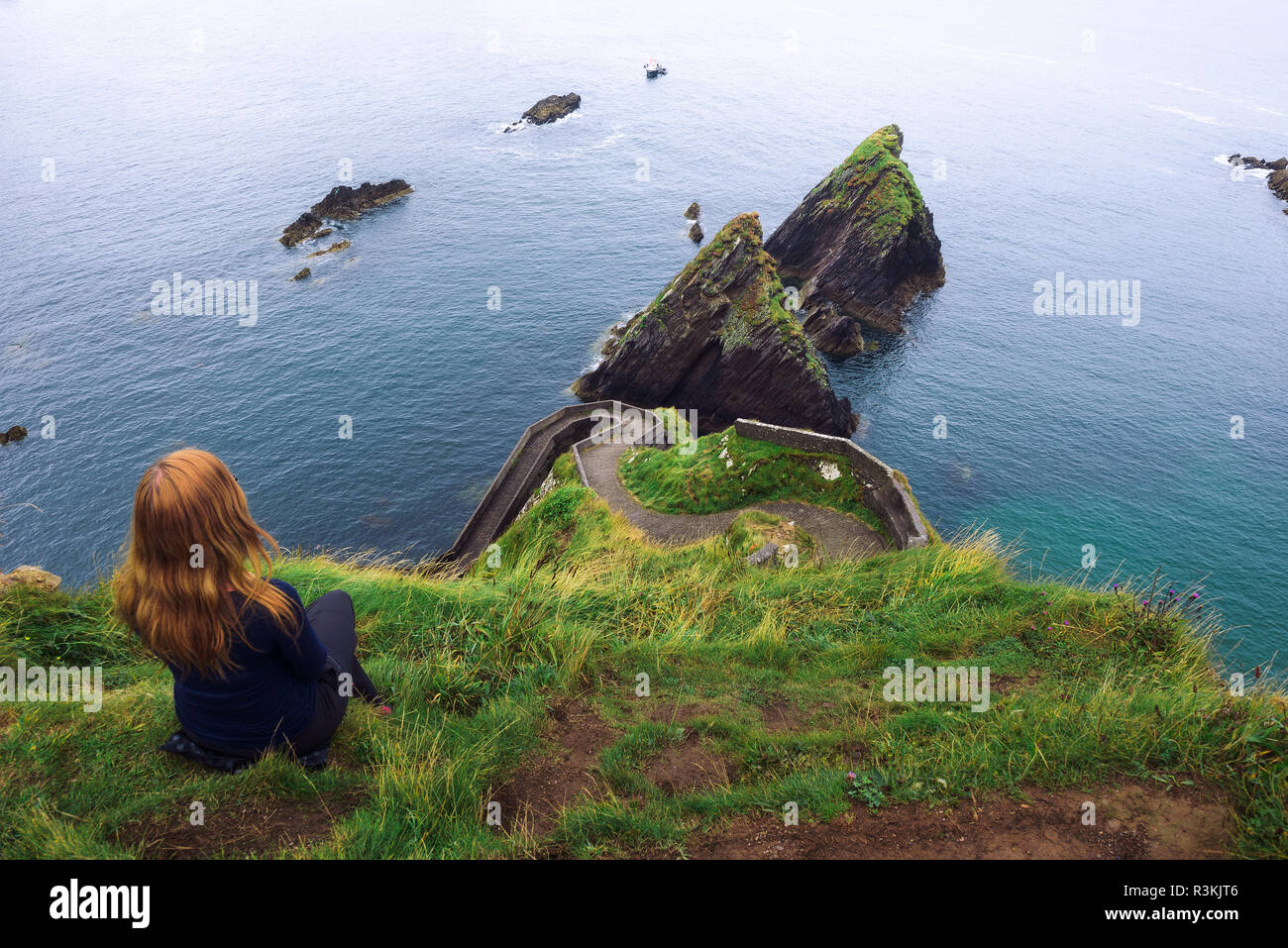 La ragazza si siede su una scogliera sopra l'oceano in Irlanda Foto Stock