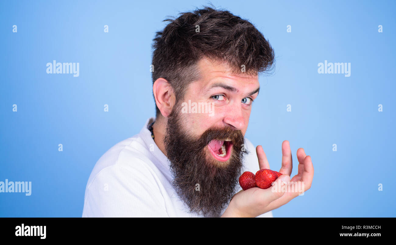 L'uomo faccia felice a bocca aperta con la barba mangia le fragole. Vuoi provare il mio berry Hipster barbuto trattiene le fragole su palm, vicino. Uomo allegro gonna Foto Stock