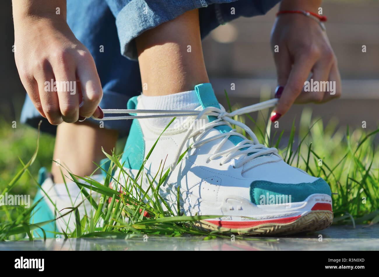 Giovane ragazza che indossa jeans legatura sui lacci delle scarpe sneakers permanente sulla verde erba vista laterale da vicino la foto in orizzontale, giornata di sole Foto Stock