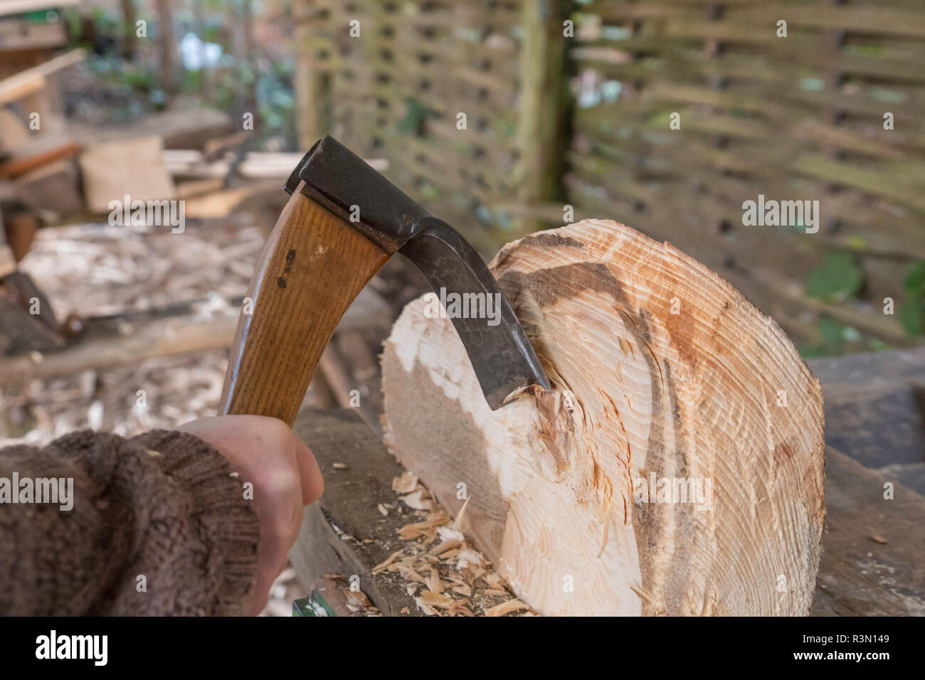 Usando una mano adze alla moda la sede per uno sgabello. Foto Stock