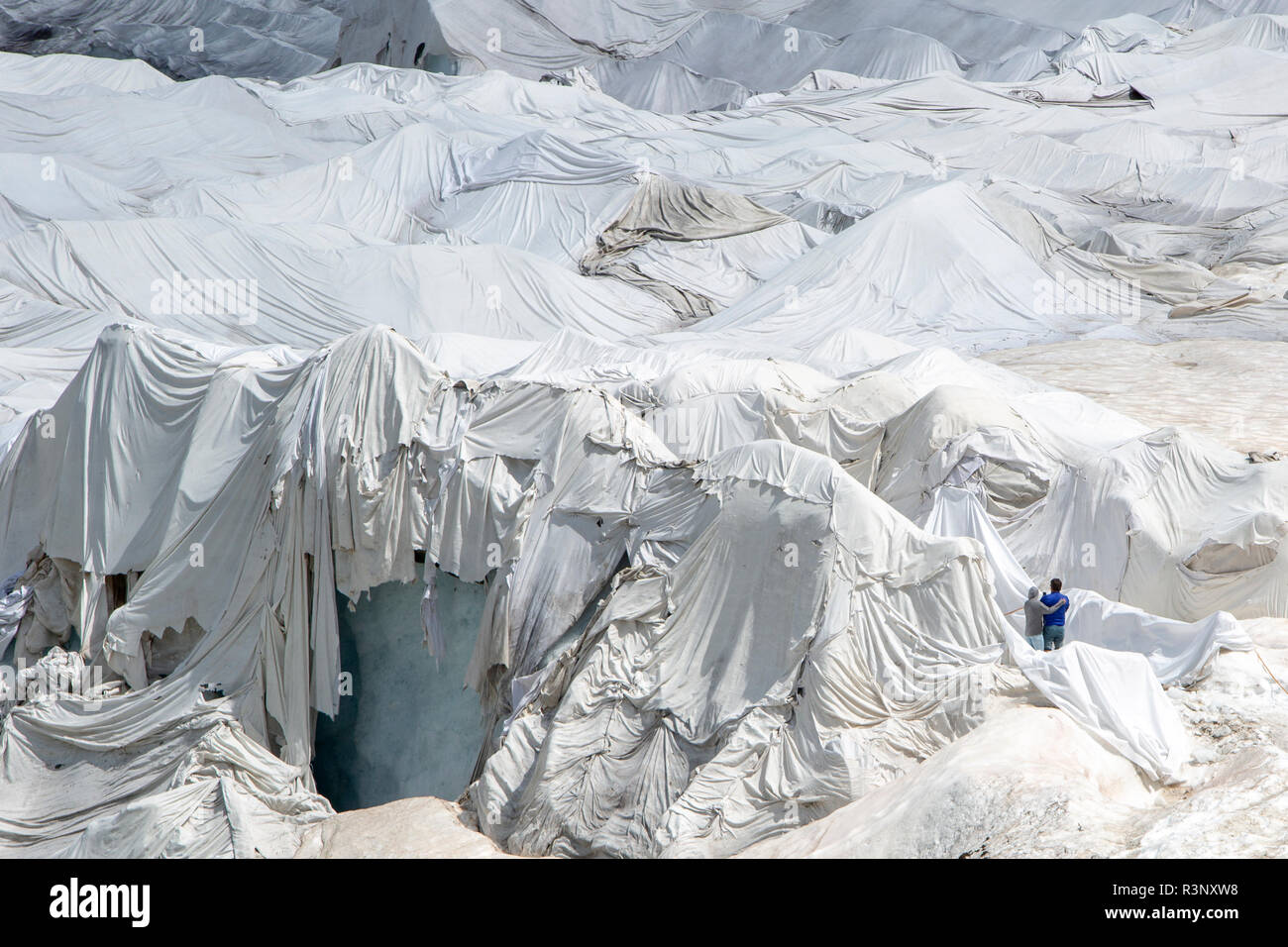 I turisti presso il ghiacciaio del Rodano in Svizzera. Dopo un inverno con un record di quantità di neve, la maggior parte di esso era andato quando questo imae è stata presa il 14 luglio 2018, esponendo il ghiaccio più scure. Mentre la neve è un brillante riflettore dell'energia dal sole, il ghiaccio più scura assorbe l'energia invece, accelerando la fusione del ghiacciaio. Il colore e le tenebre del ghiacciaio variano in tutto il mondo, a seconda dell'accumulo di inquinamento, età di ghiaccio, particelle prelevate dal ghiaccio e dai microrganismi nel ghiaccio. Il ghiacciaio è però raramente bianca come la neve. Con inverni brevi e vanishing snow cove Foto Stock