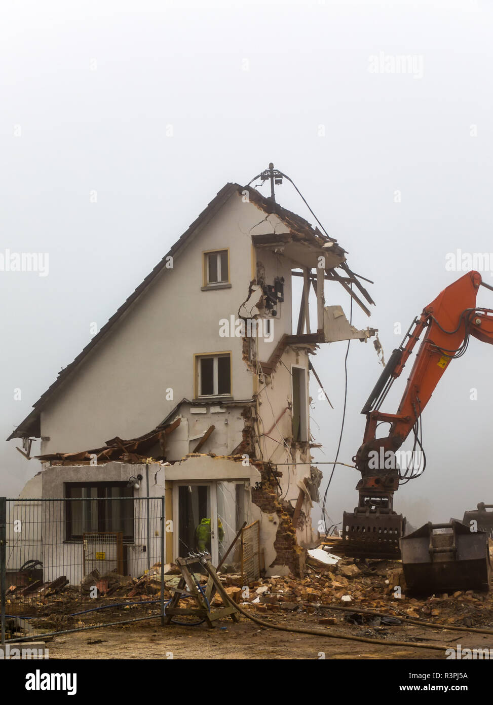Escavatore bulldozer demolendo il vecchio edificio residenziale su un nebbioso giorno Foto Stock