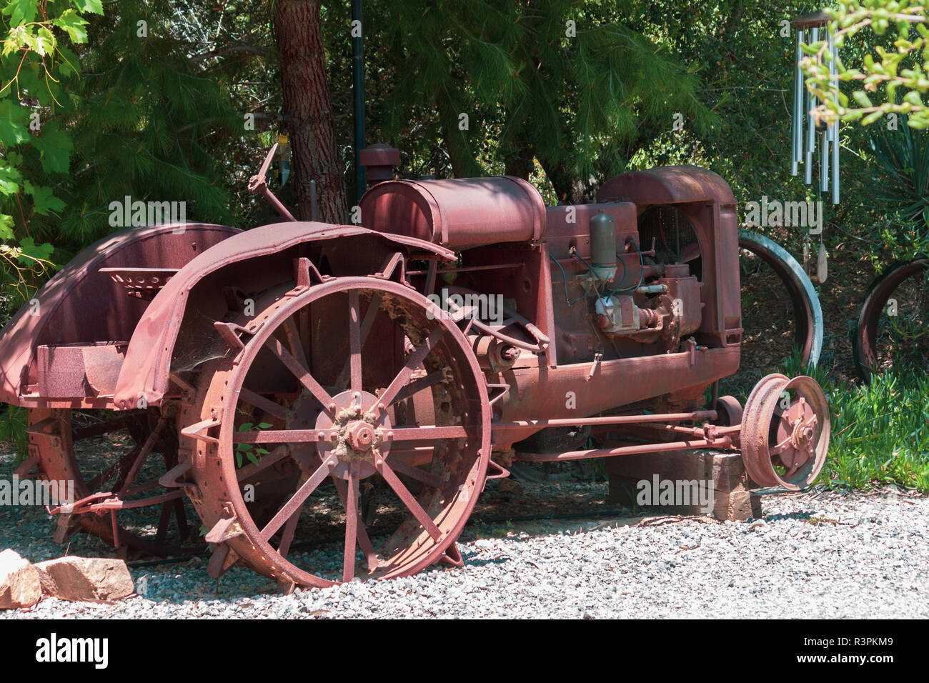 Depressione era arrugginito antichi ruota in acciaio trattore agricolo si è ritirato nel quadro di una shade tree Foto Stock