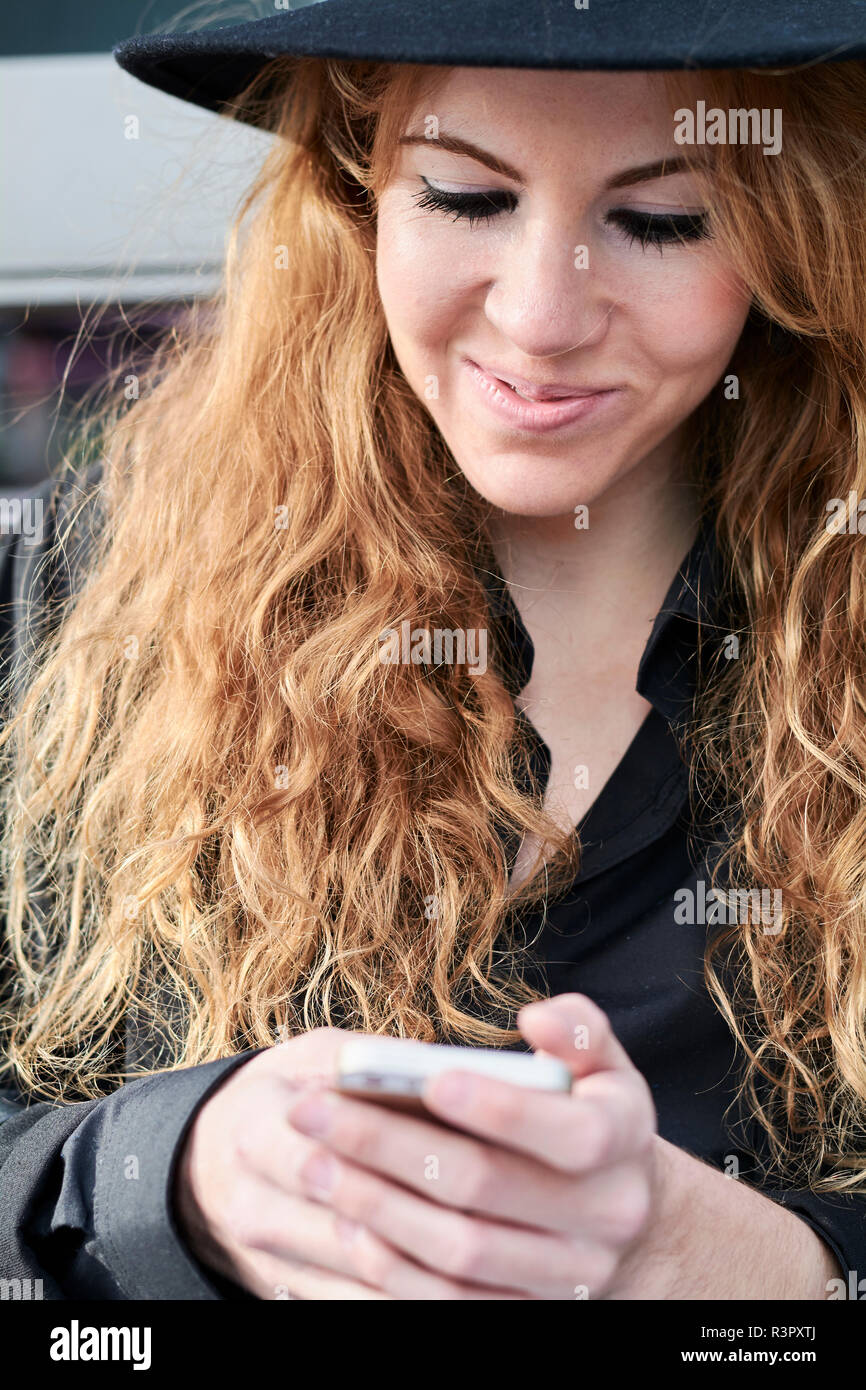 Metà donna adulta indossando black hat e utilizza lo smartphone Foto Stock