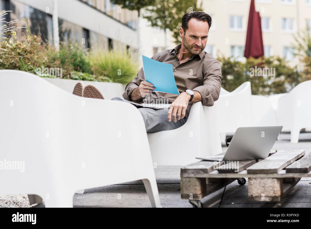 Uomo con documenti seduti sulla terrazza che guarda al laptop Foto Stock