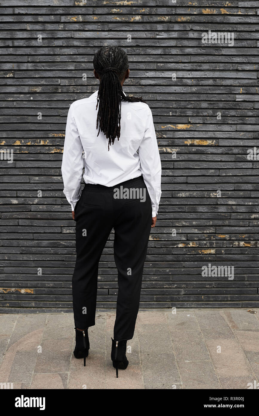 Vista posteriore di imprenditrice con dreadlocks che indossa una camicia bianca e pantaloni neri Foto Stock