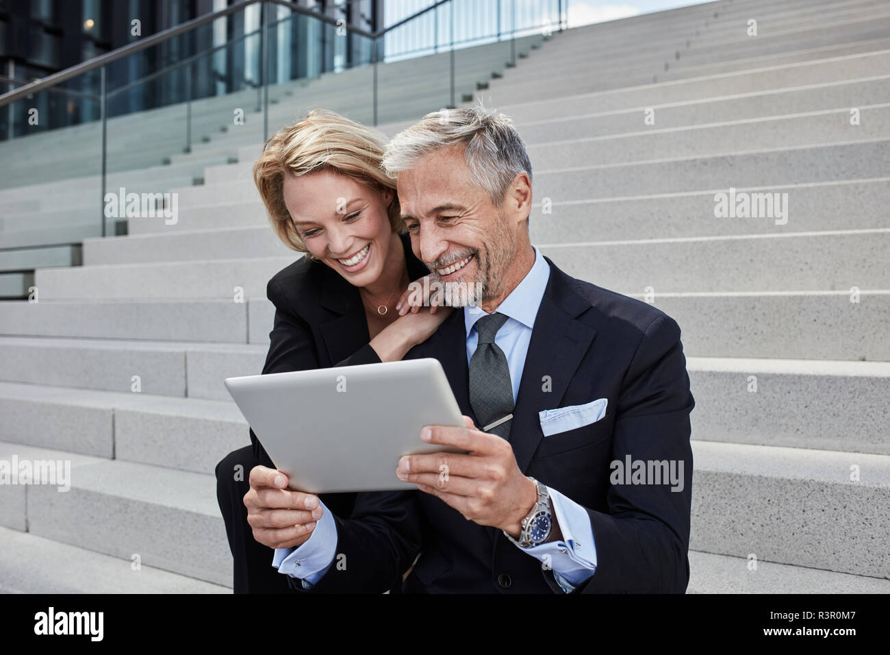 Ritratto di due imprenditori ridere seduti insieme su scale guardando tablet Foto Stock