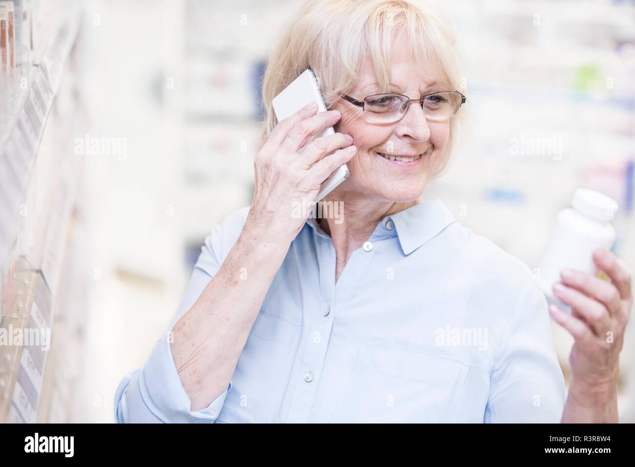Senior donna discutendo la medicina sul telefono cellulare in farmacia. Foto Stock