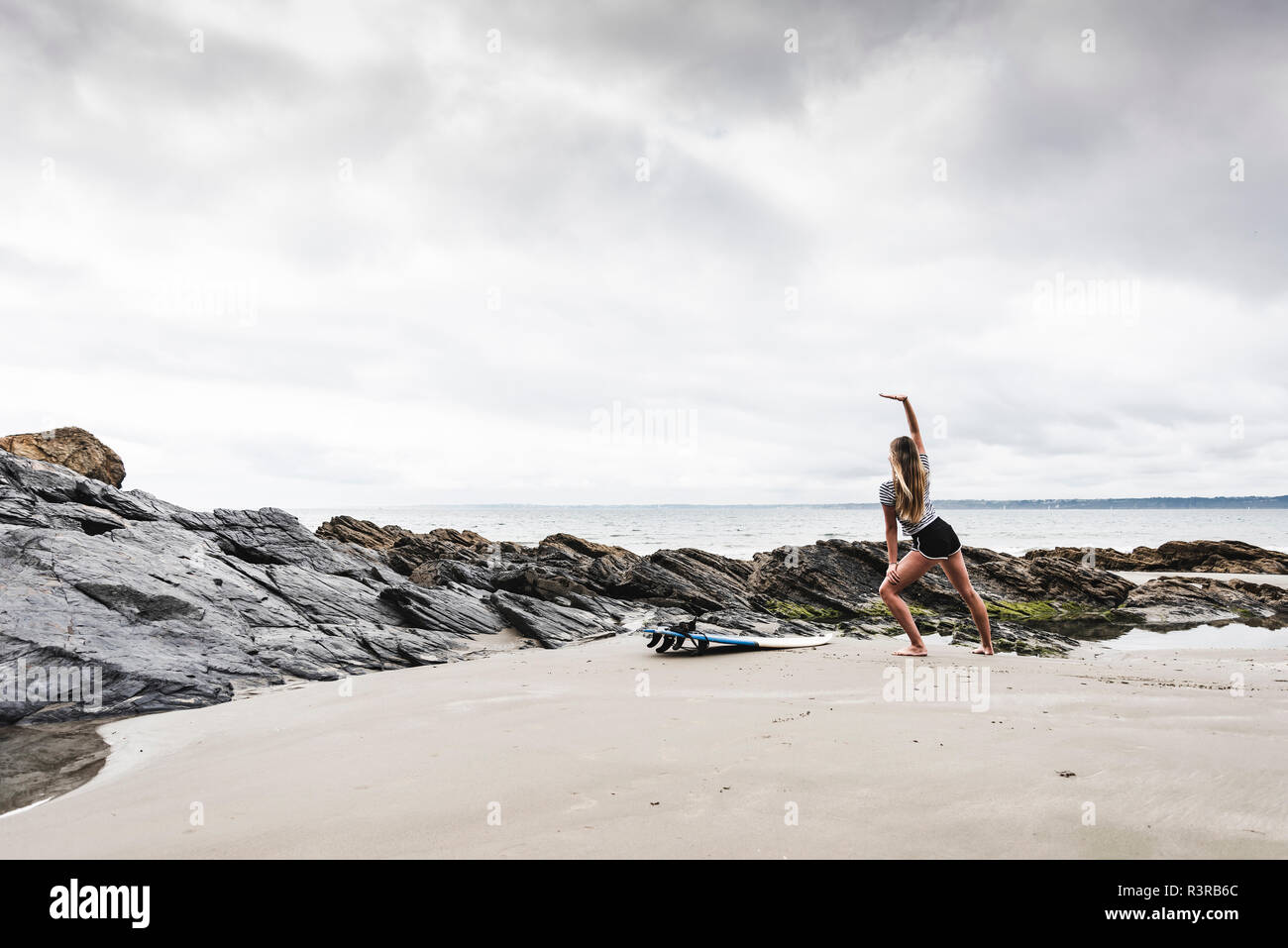 Giovane donna con la tavola da surf stretching sulla spiaggia Foto Stock