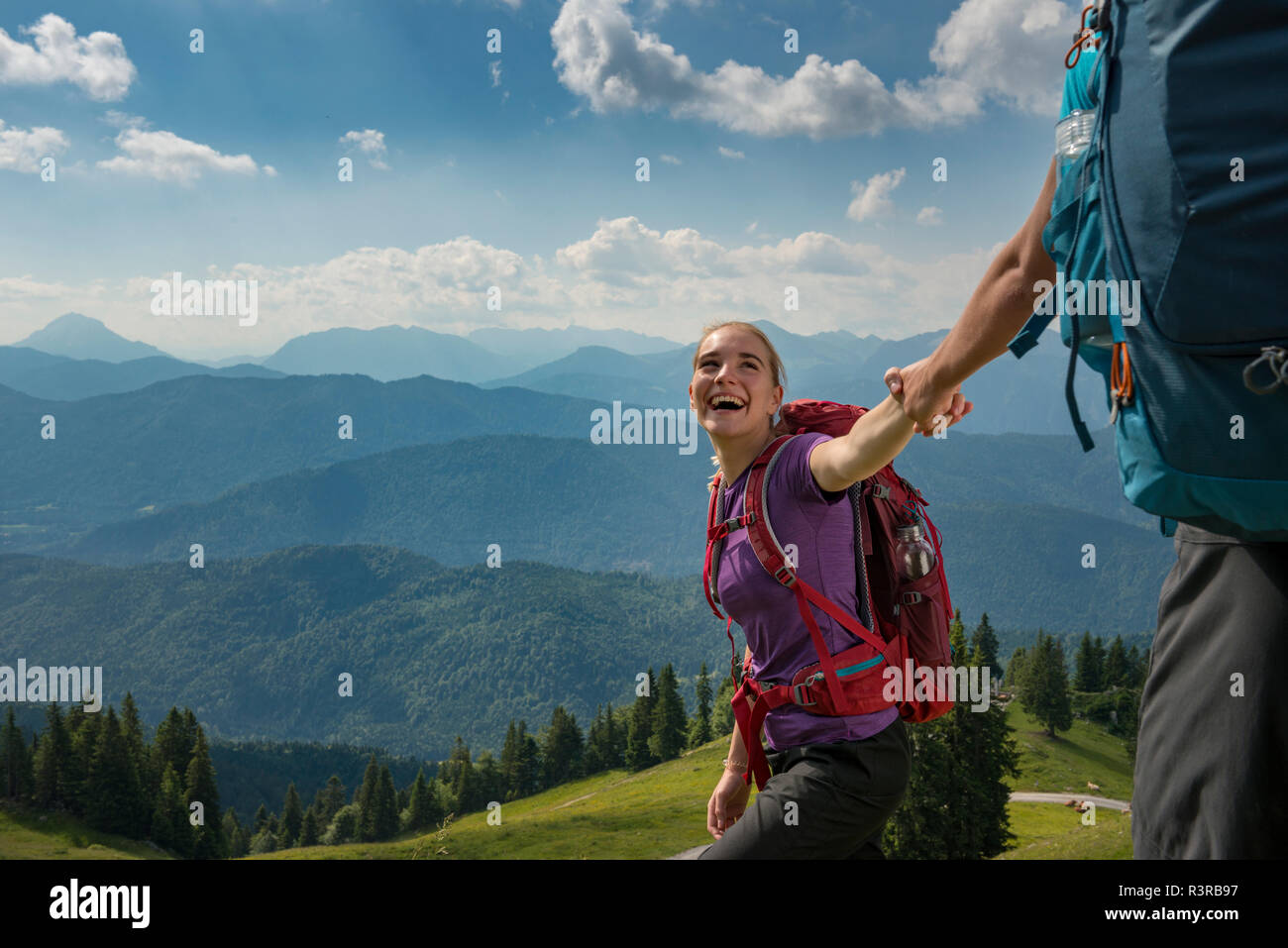 In Germania, in Baviera, vicino Brauneck Lenggries, felice giovane donna escursioni nel paesaggio alpino tenendo la mano del fidanzato Foto Stock