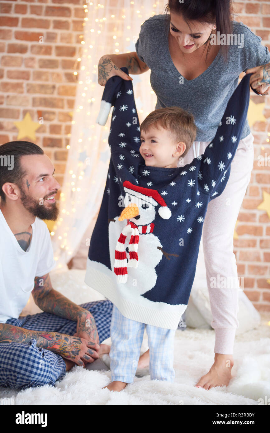 Ragazzo cerca su sovradimensionato maglione di Natale con i genitori in letto Foto Stock