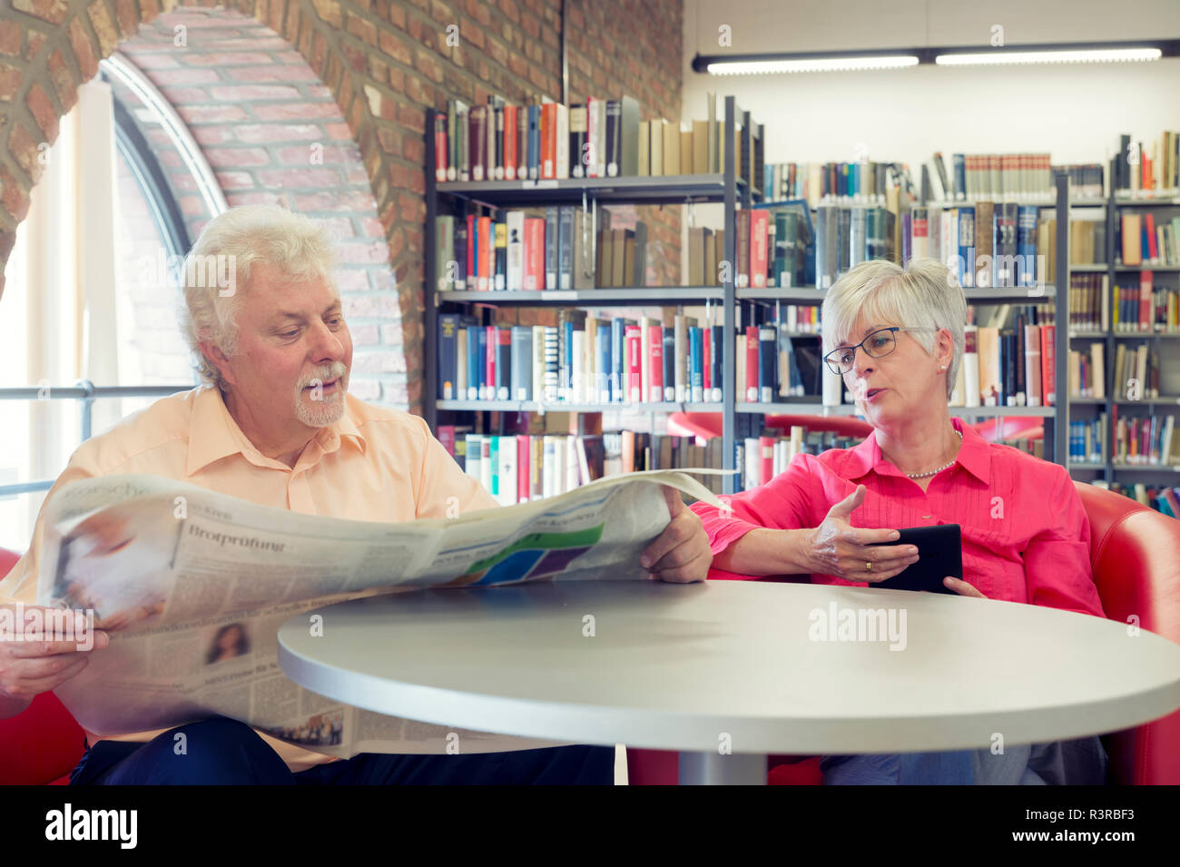 Ein Seniorenpaar in einer Bibliothek mit Zeitung und Kindle. Grevenbroich, Nordrhein-Westfalen, Deutschland Foto Stock