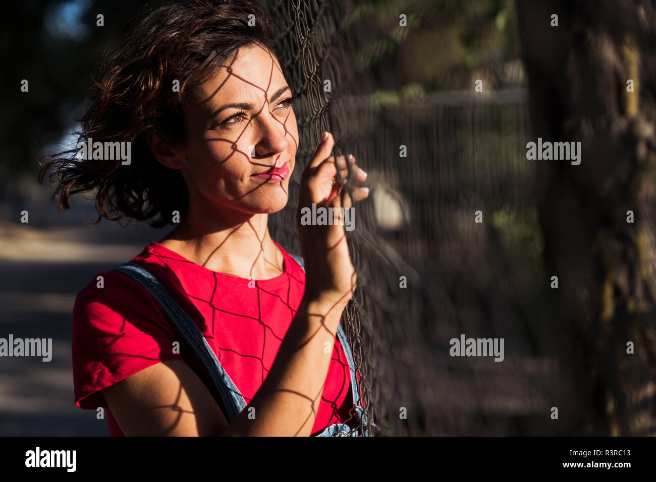 Ritratto di donna sorridente con ombra di recinto di maglia di filo sulla sua faccia rivolta a distanza Foto Stock