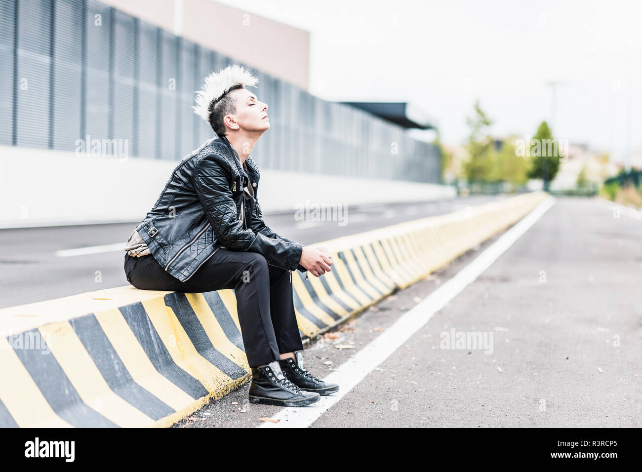 Punk donna seduta al bordo della strada con gli occhi chiusi Foto Stock
