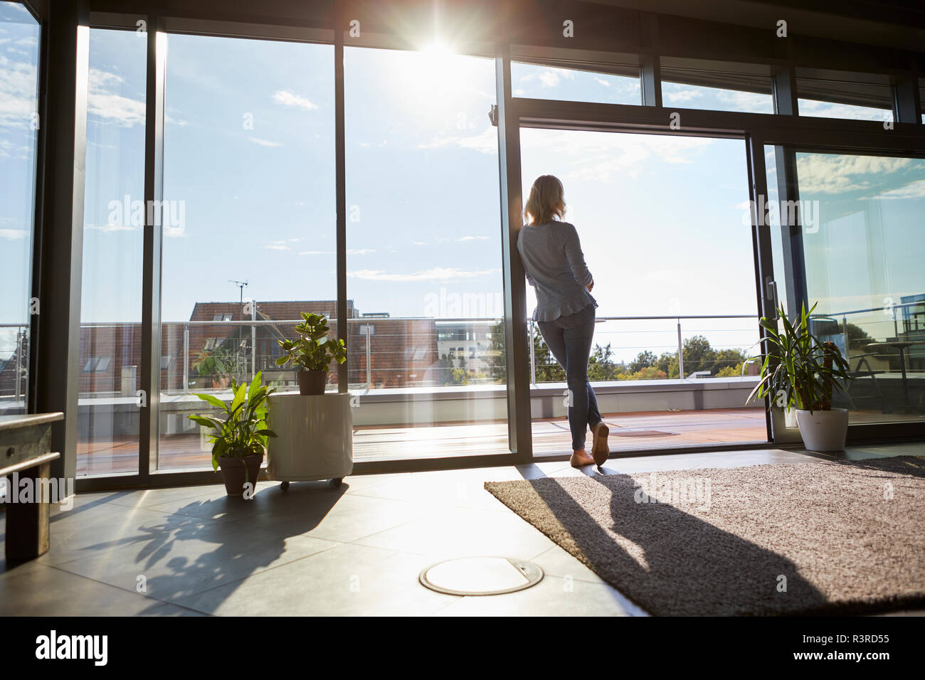 Vista posteriore della donna in controluce in piedi presso la finestra a casa guardando fuori Foto Stock