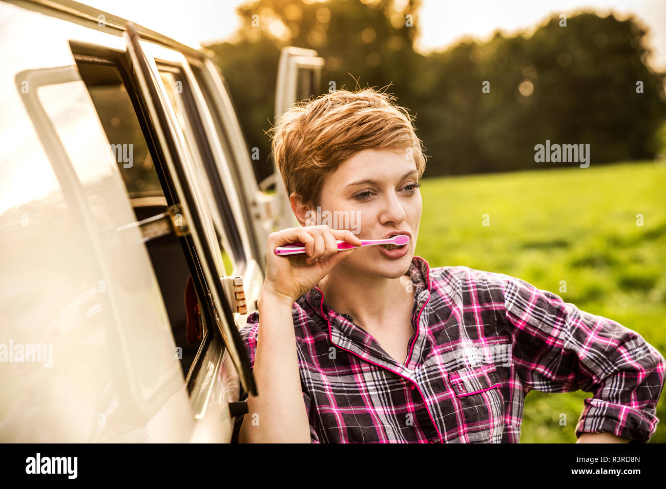 La donna in pigiama spazzolare i denti in un furgone nel paesaggio rurale Foto Stock