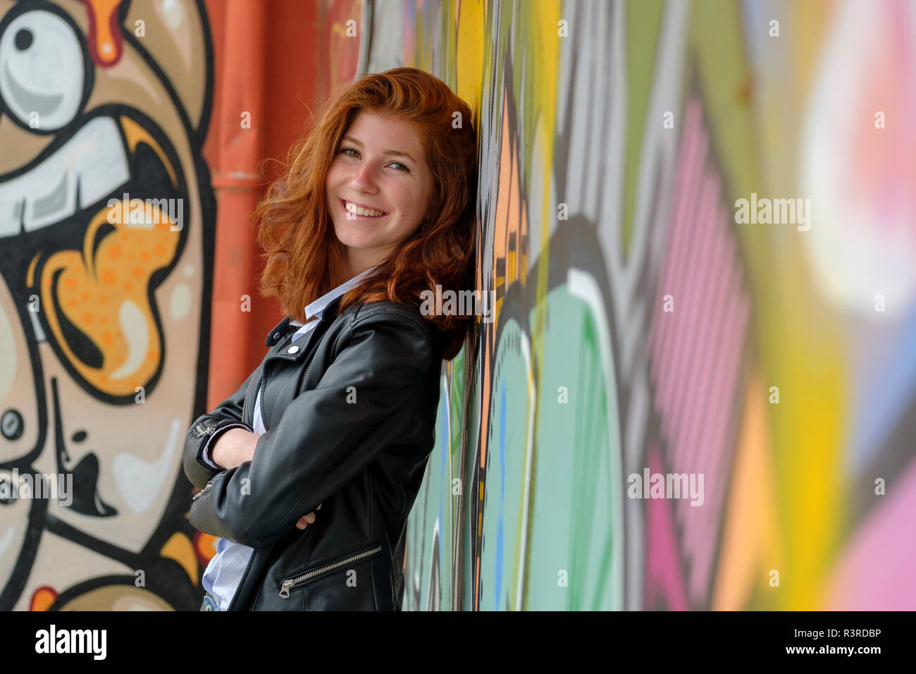 L'Italia, Finale Ligure, ritratto di sorridente ragazza adolescente appoggiata contro il murale Foto Stock