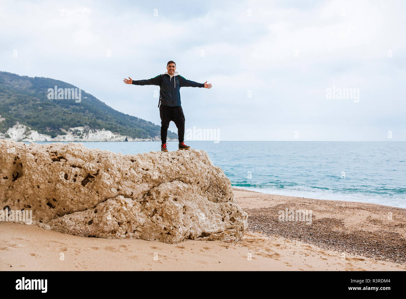L'Italia, Vieste, rilassato uomo con le braccia aperte in piedi su una roccia sulla spiaggia di Vignanotica Foto Stock