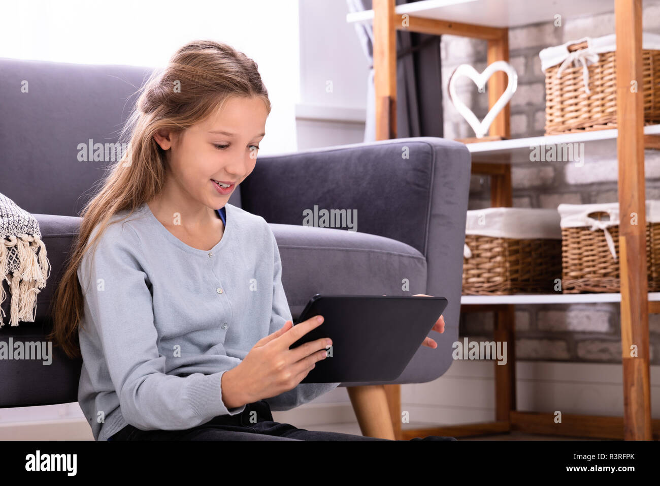 Ragazza seduta nella parte anteriore del divano con tavoletta digitale in casa Foto Stock