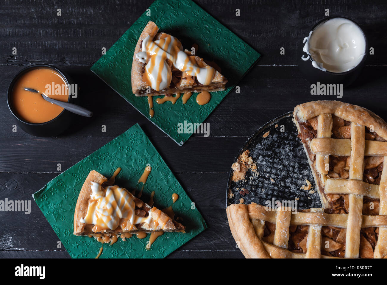 Vista dall'alto di una tabella con tutta una fetta di torta di mele e due fette su tovaglioli, decorato con caramello e panna montata. Dolci fatti in casa il cibo. Foto Stock