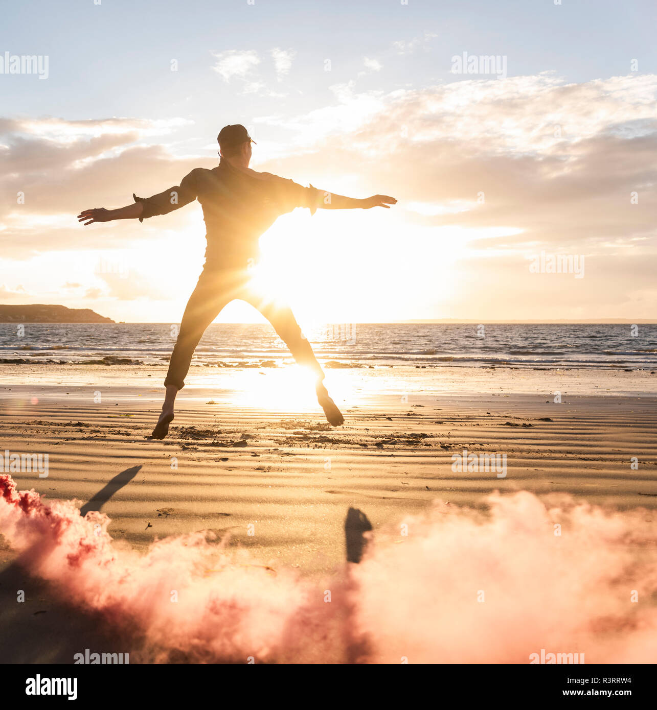 Uomo che fa del movimento di formazione presso la spiaggia con fumo colorato al tramonto Foto Stock