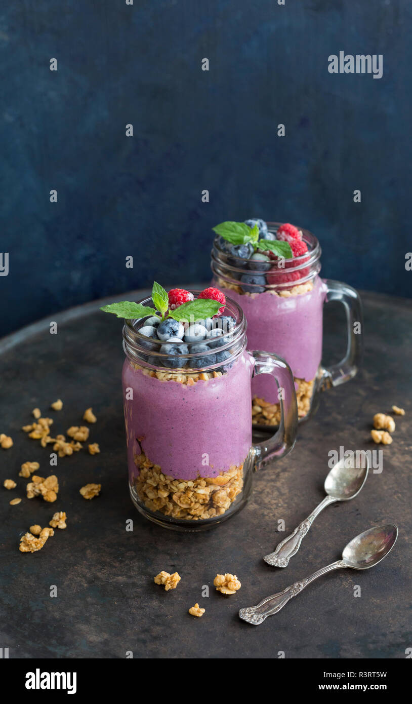 Due bicchieri di yogurt con muesli di arachidi, aronia polvere e topping di granella di nocciole e frutti di bosco surgelati Foto Stock