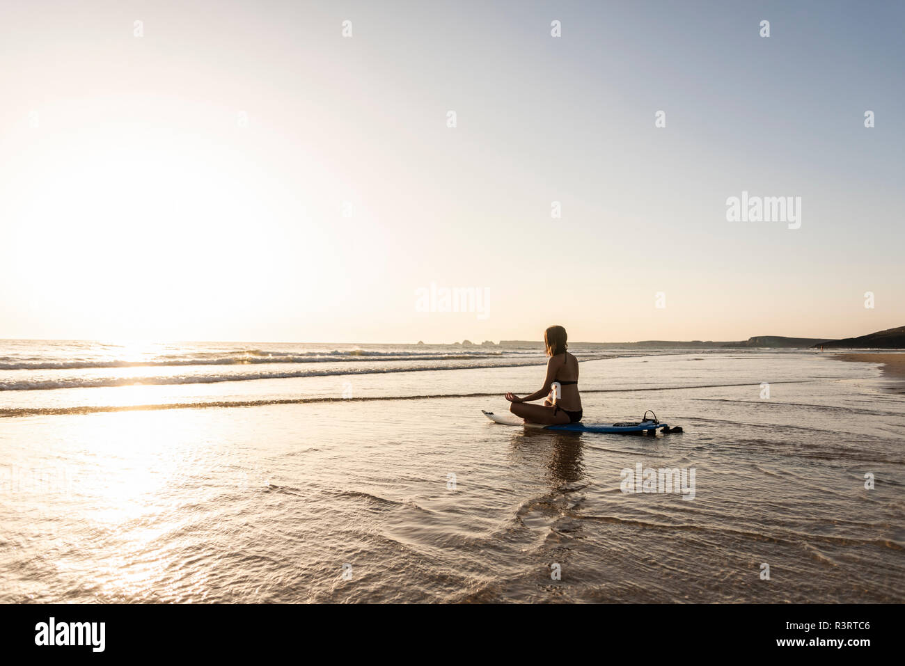Giovane donna a praticare yoga sulla spiaggia, seduti su una tavola da surf, meditando Foto Stock
