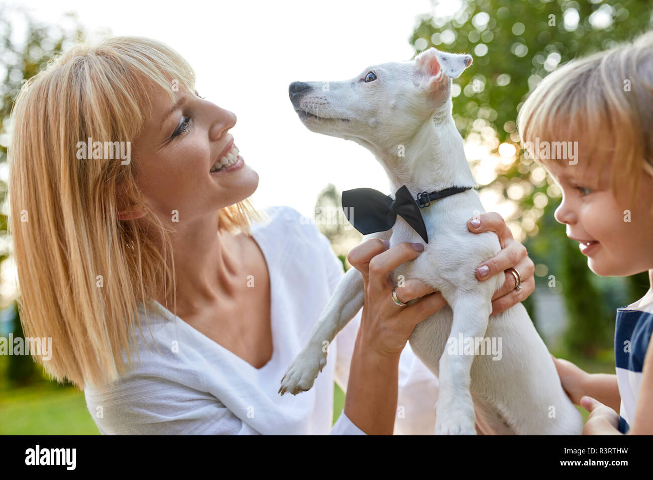 Donna felice con la figlia tenendo il cane che indossa una cravatta a farfalla all'aperto Foto Stock
