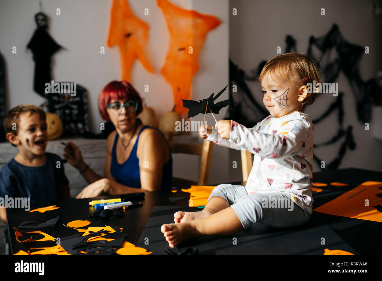 Baby girl giocando con decorazione di halloween a casa mentre la madre e il fratello osservando il suo Foto Stock
