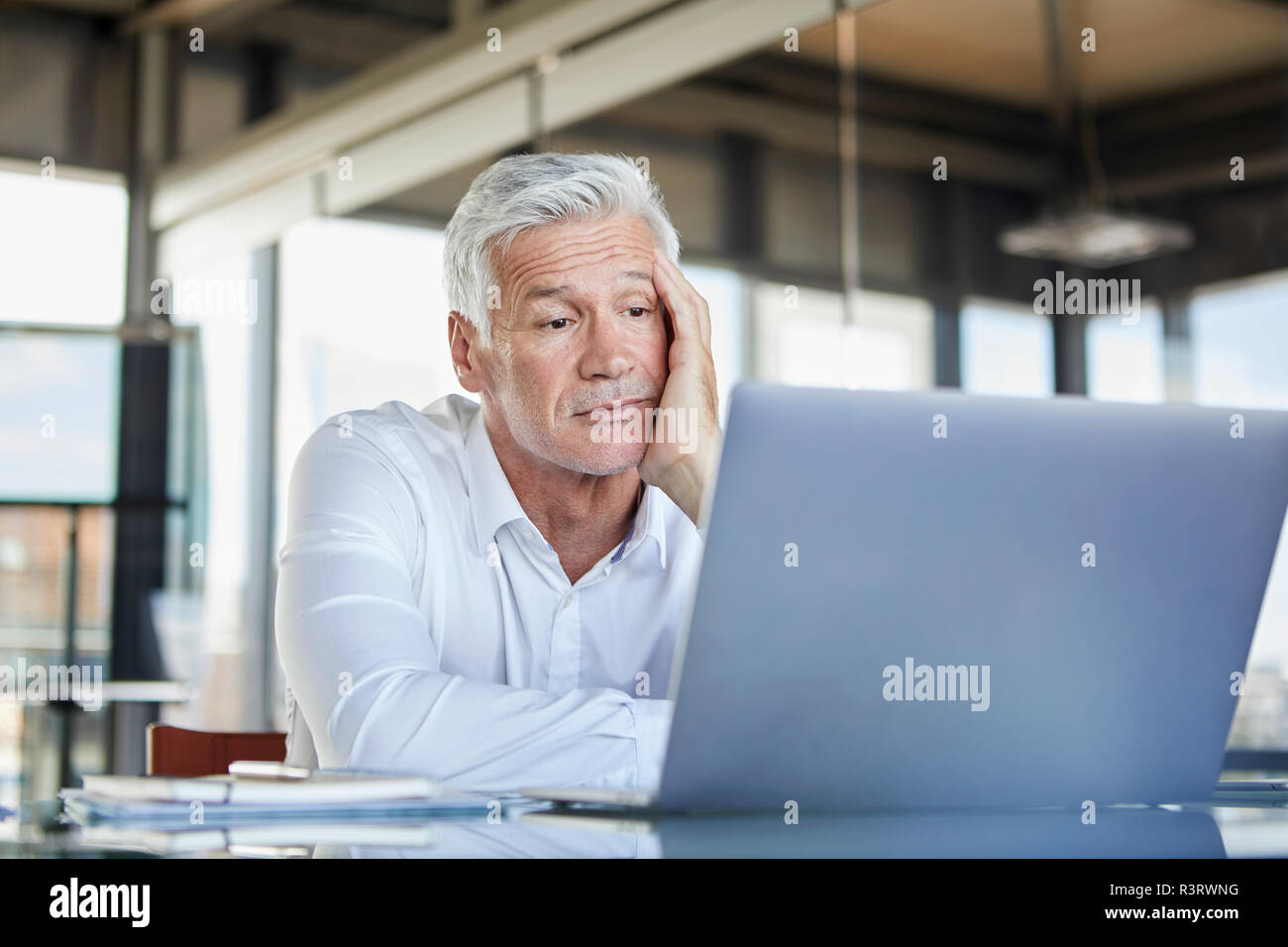 Imprenditore annoiato seduto alla scrivania, utilizzando laptop Foto Stock
