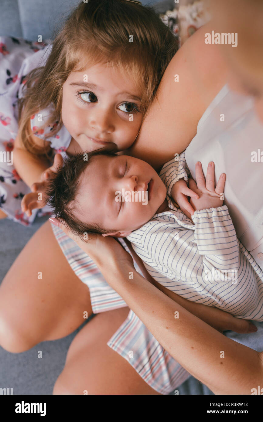 Madre tenendo il suo bambino vicino con la sorella sensazione i suoi capelli Foto Stock