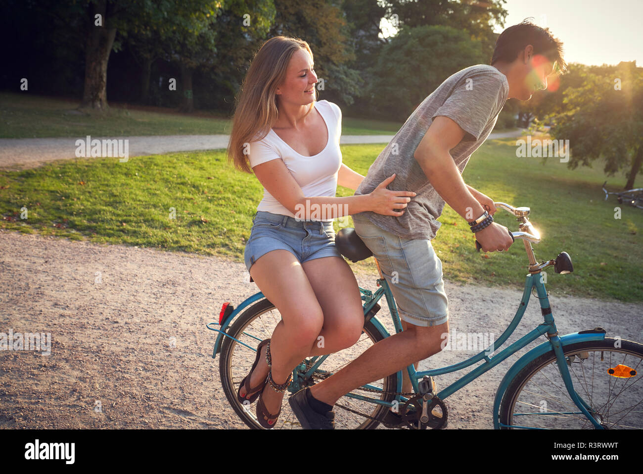 Coppia giovane equitazione bicicletta nel parco, donna seduta su rack Foto Stock