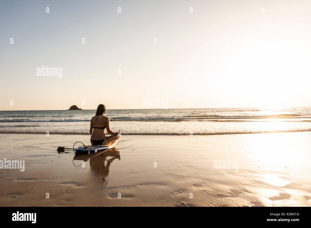 Giovane donna a praticare yoga sulla spiaggia, seduti su una tavola da surf, meditando Foto Stock