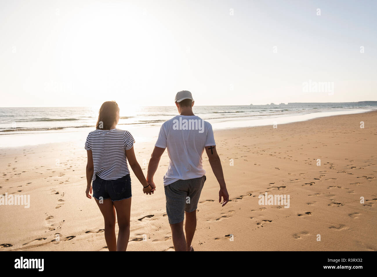 Coppia giovane fare una romantica passeggiata sulla spiaggia al tramonto Foto Stock