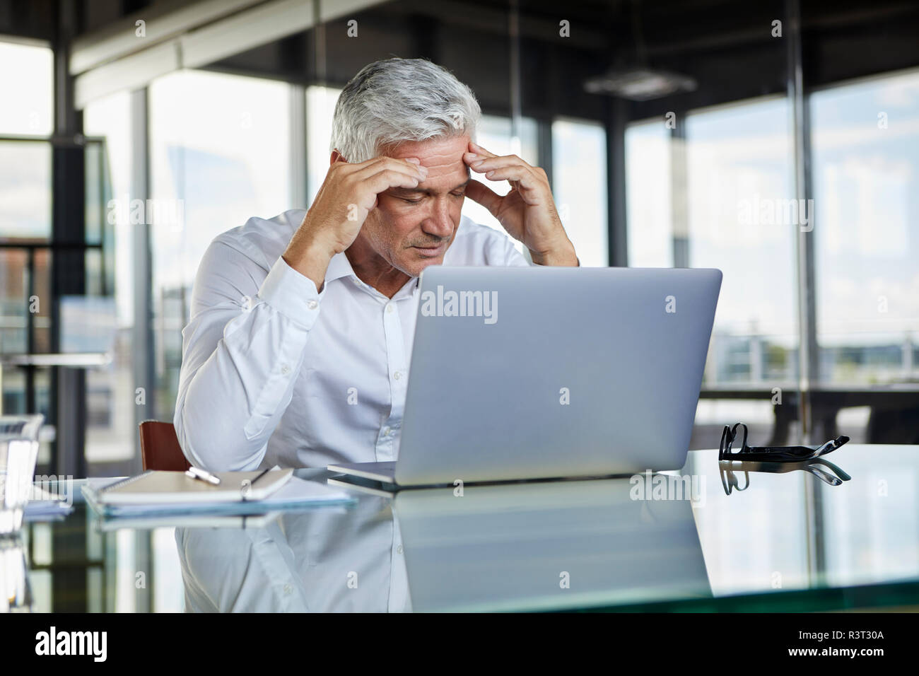Sottolineato imprenditore seduto alla scrivania con computer portatile, tenendo la sua testa Foto Stock