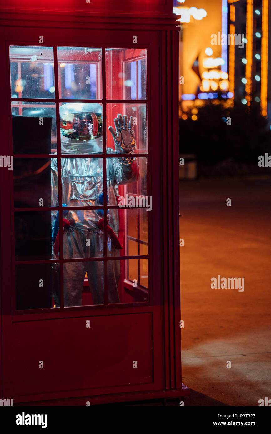 Spaceman in piedi in una cabina telefonica di notte Foto Stock