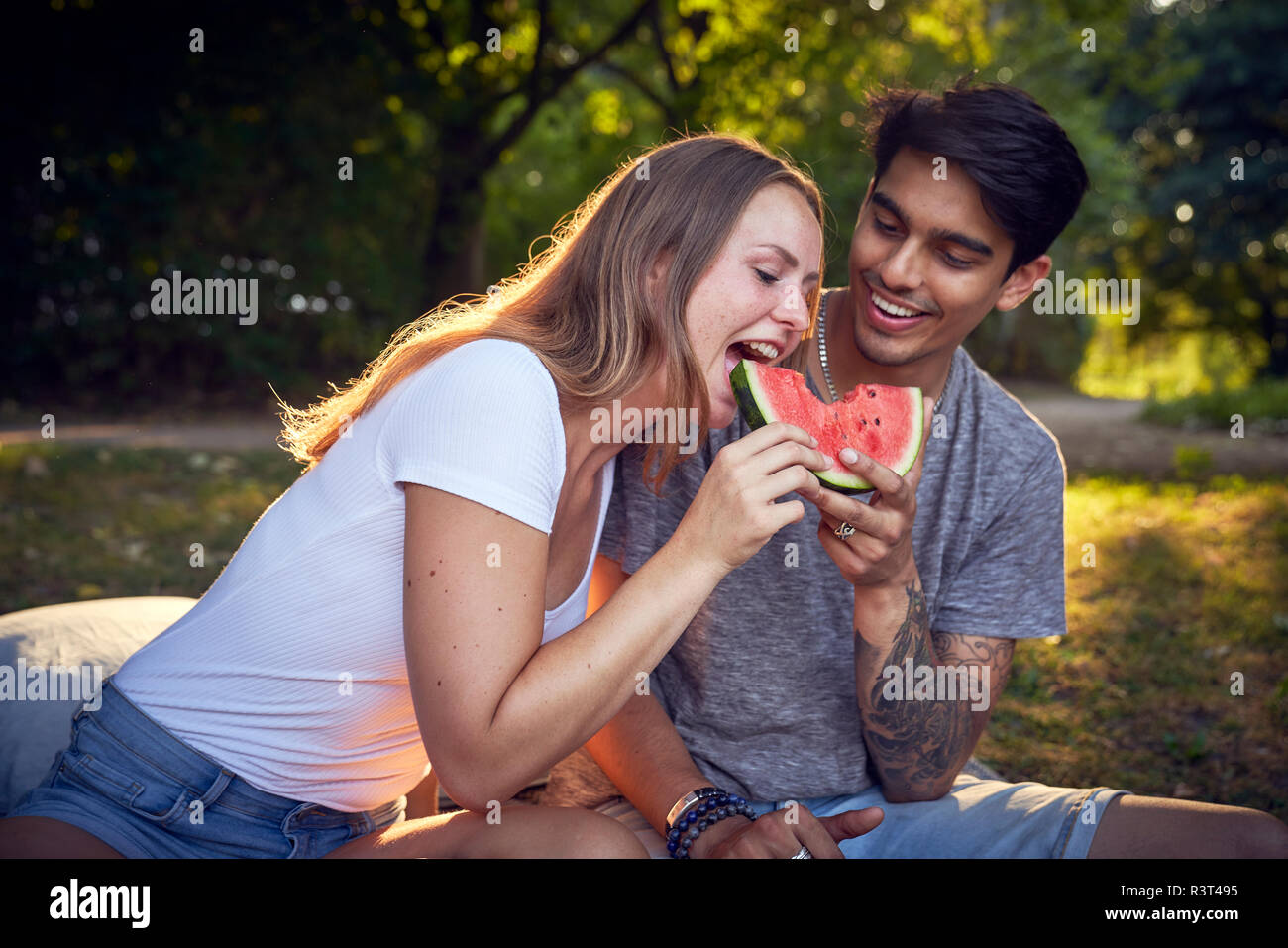 Coppia giovane seduto nel parco, mangiando anguria Foto Stock