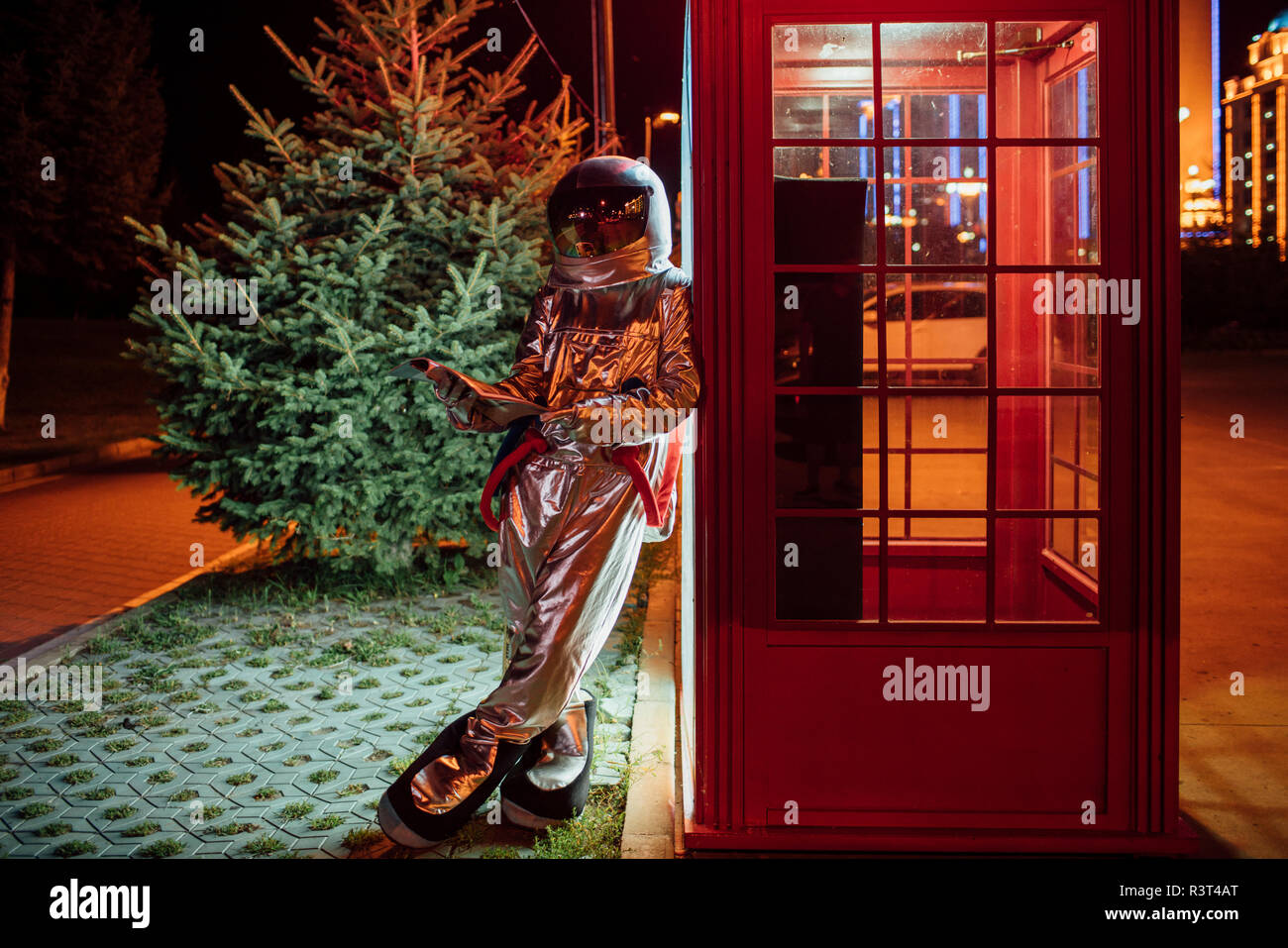 Spaceman appoggiata contro un telefono casella di notte la lettura del libro di telefono Foto Stock