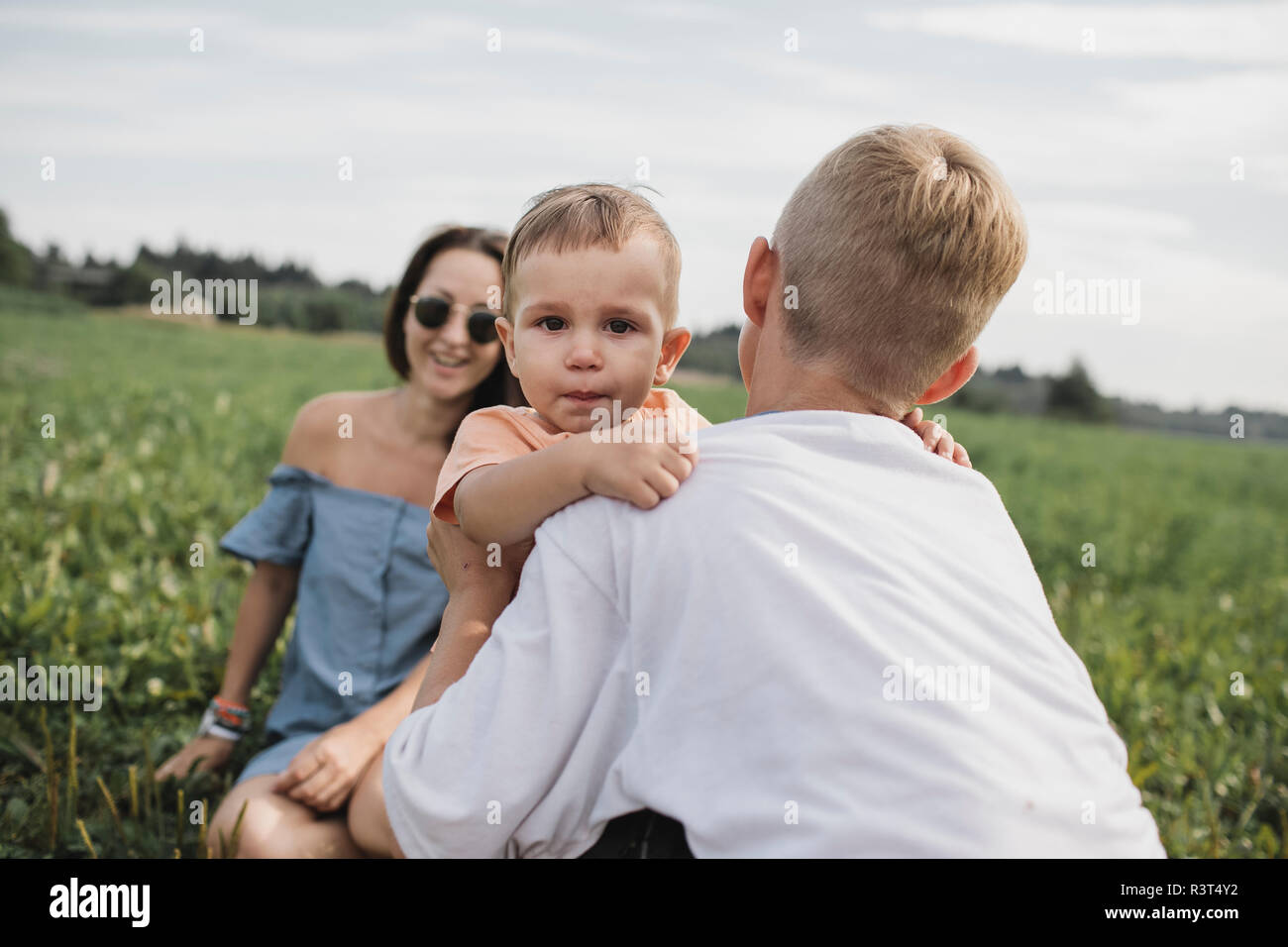 Fratello consolante Gridando bambino su un campo con la madre in background Foto Stock
