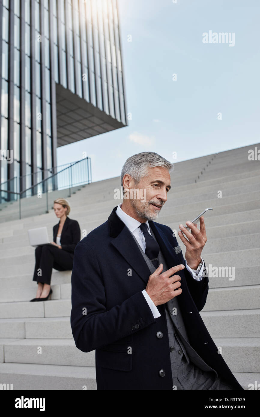 Ritratto di imprenditore a parlare al telefono mentre business donna lavora sul computer portatile in background Foto Stock