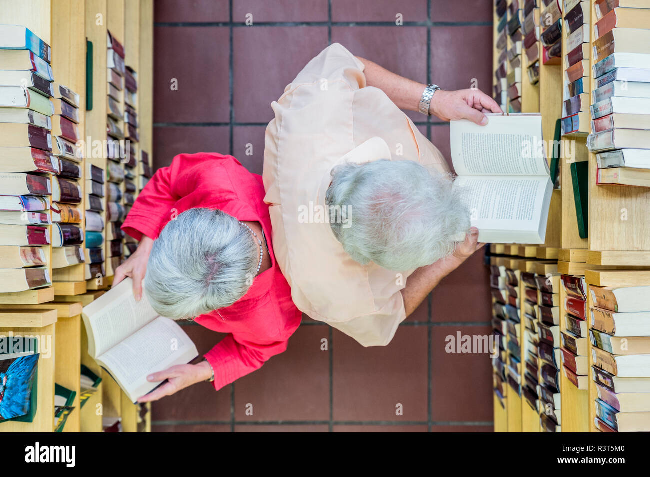 Ein Senior und eine Seniorin stehen Rücken un Rücken zwischen Bücherregalen. Draufsicht. Grevenbroich, Nordrhein-Westfalen, Deutschland Foto Stock