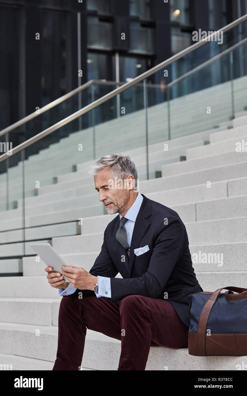Moda uomo d affari con borsa da viaggio seduti sulle scale utilizzando tablet Foto Stock
