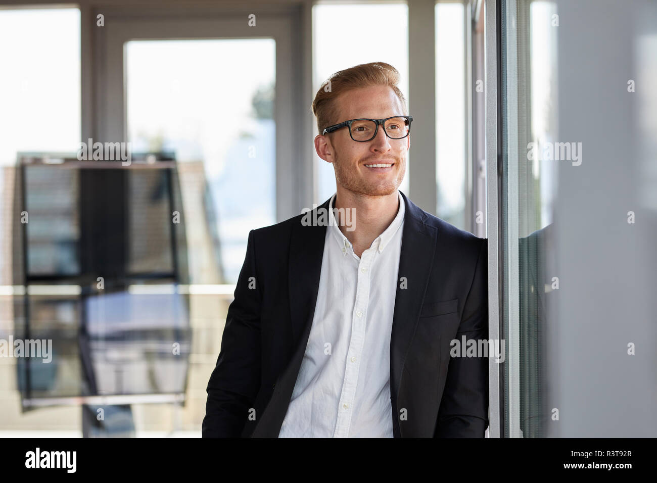 Imprenditore sorridente in ufficio guardando fuori della finestra Foto Stock